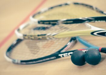 Three squash rackets and two squash balls lying on a squash court